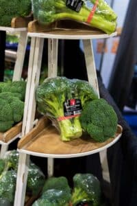 Bundles of broccoli wrapped in plastic are displayed on a tiered wooden stand.