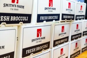 Stacks of white boxes labeled "Smith's Farm Stag Brand Fresh Broccoli" are arranged in a row.